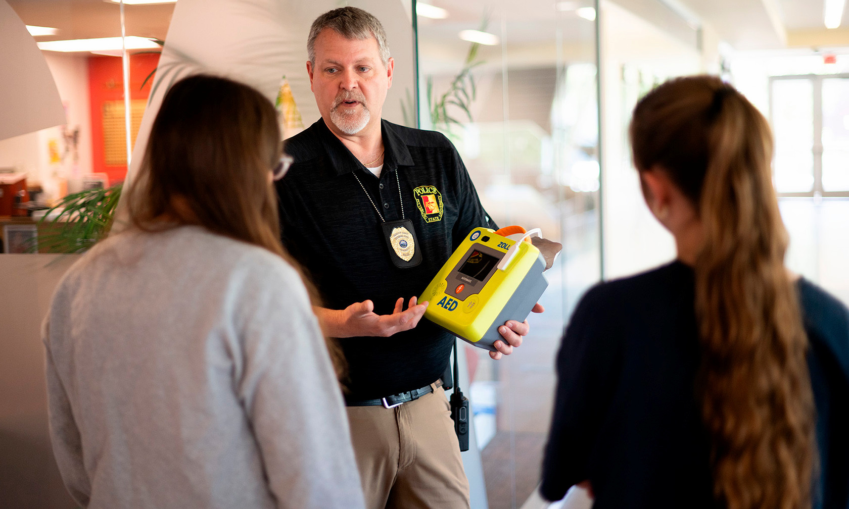 officer holding AED and explaining it to students