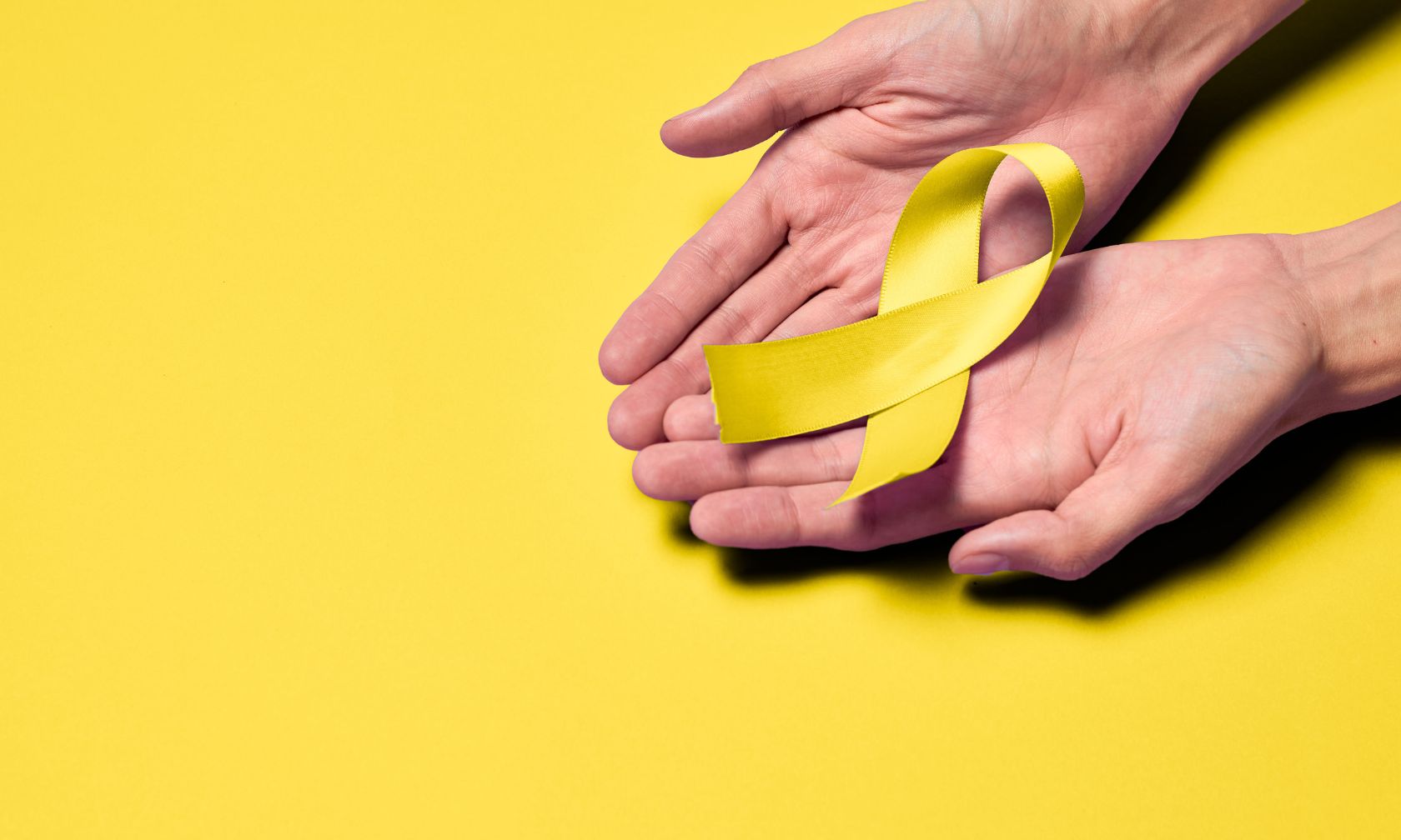 Two hands holding out a yellow ribbon.