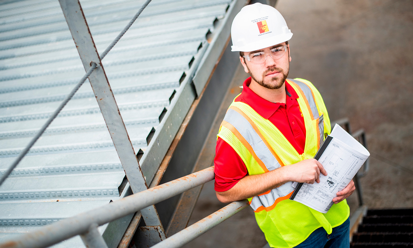 student wearing hardhat and holding blueprints