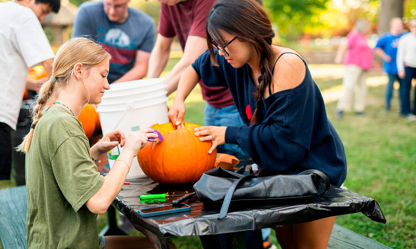 international student and American student carving a pumpkin outside