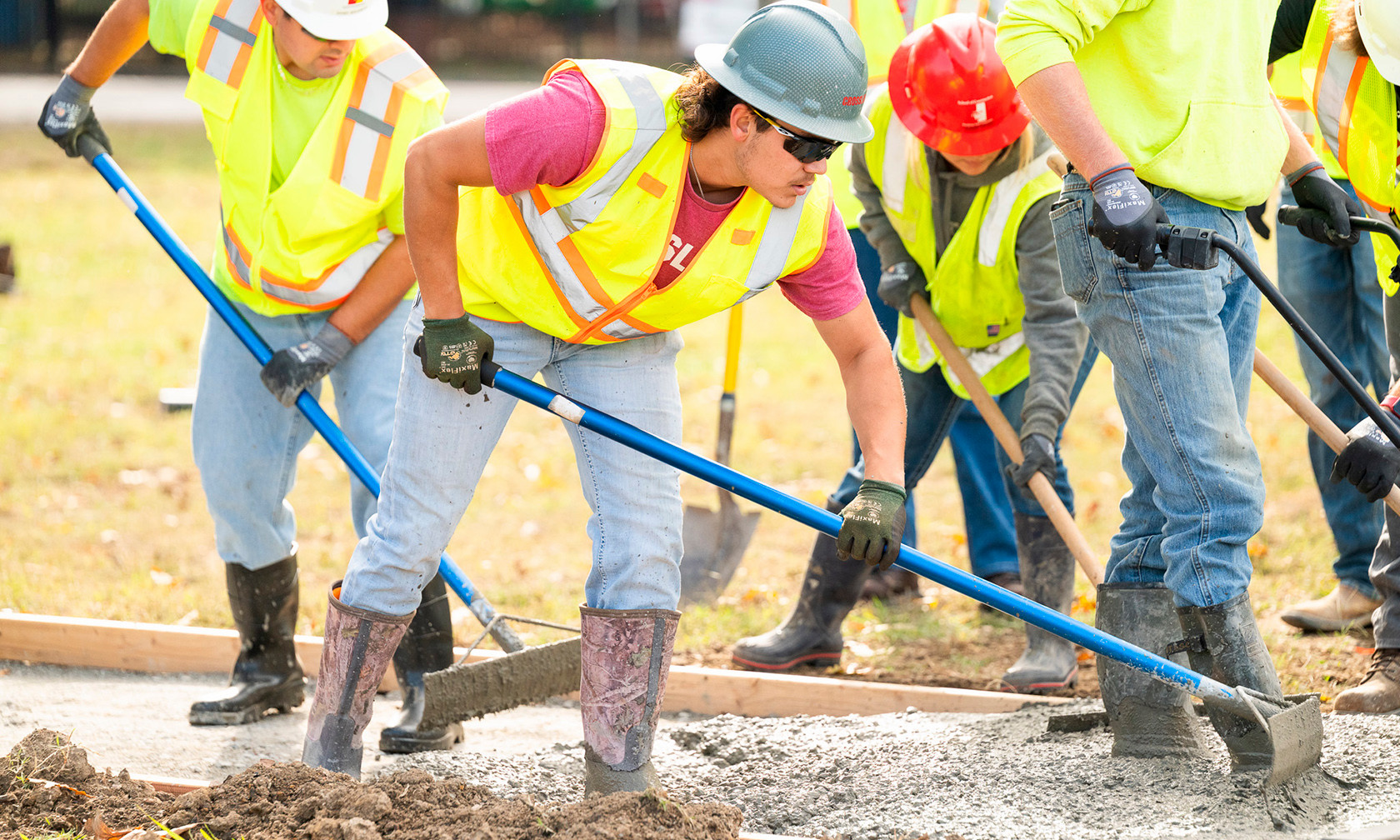 Students in hard hats using tools to build concrete sidewalk