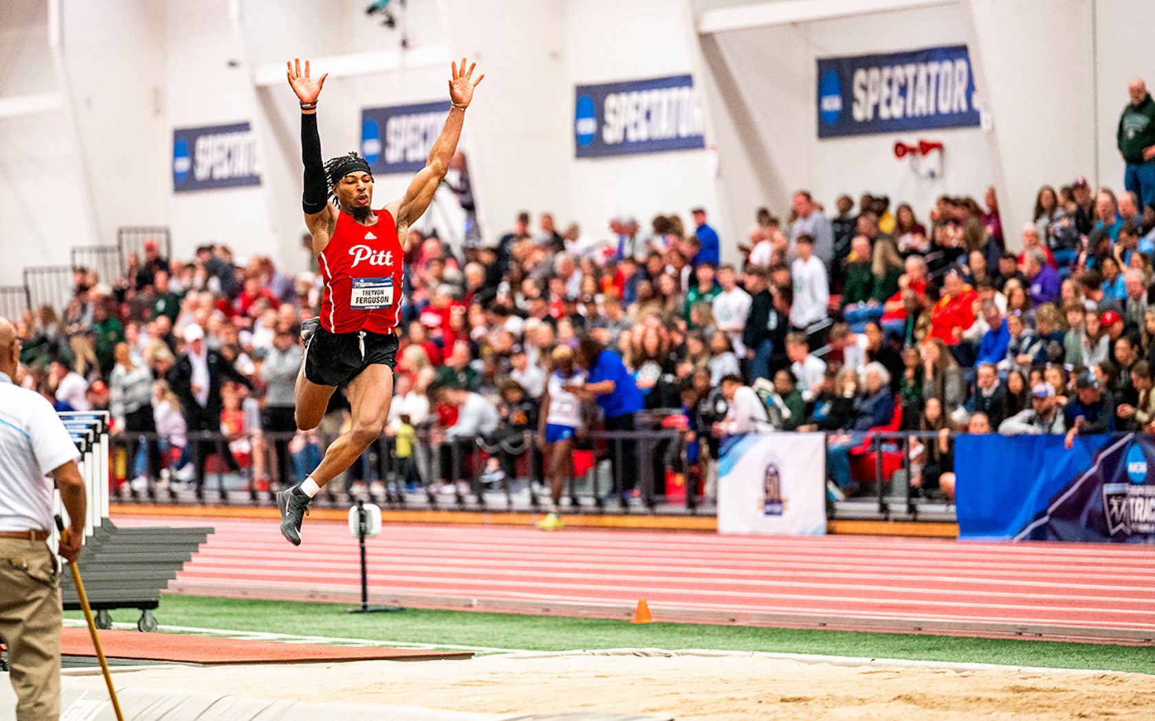 athlete doing long jump in indoor facility with big crowd watching