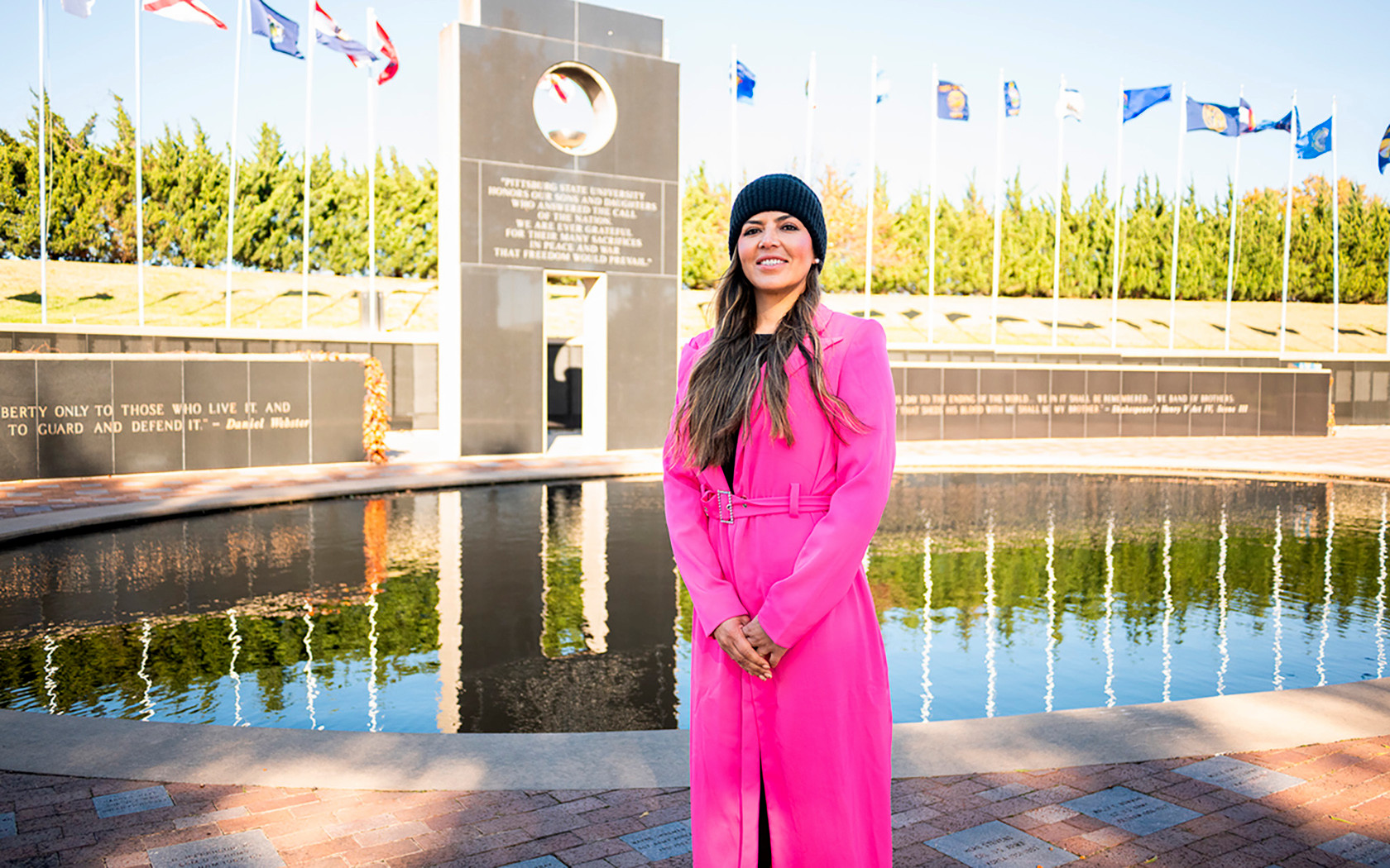 female veteran standing in front of a reflecting pool at a veterans memorial with flags in background