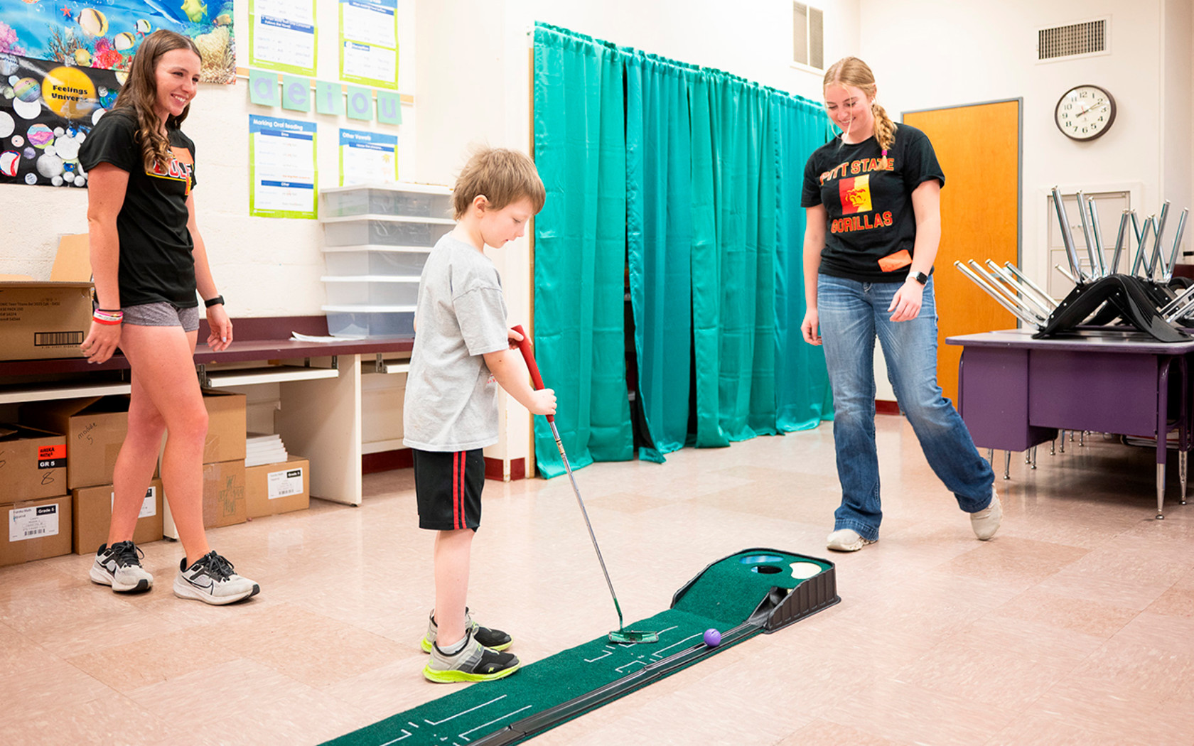 members of the golf team playing golf with a child at a school