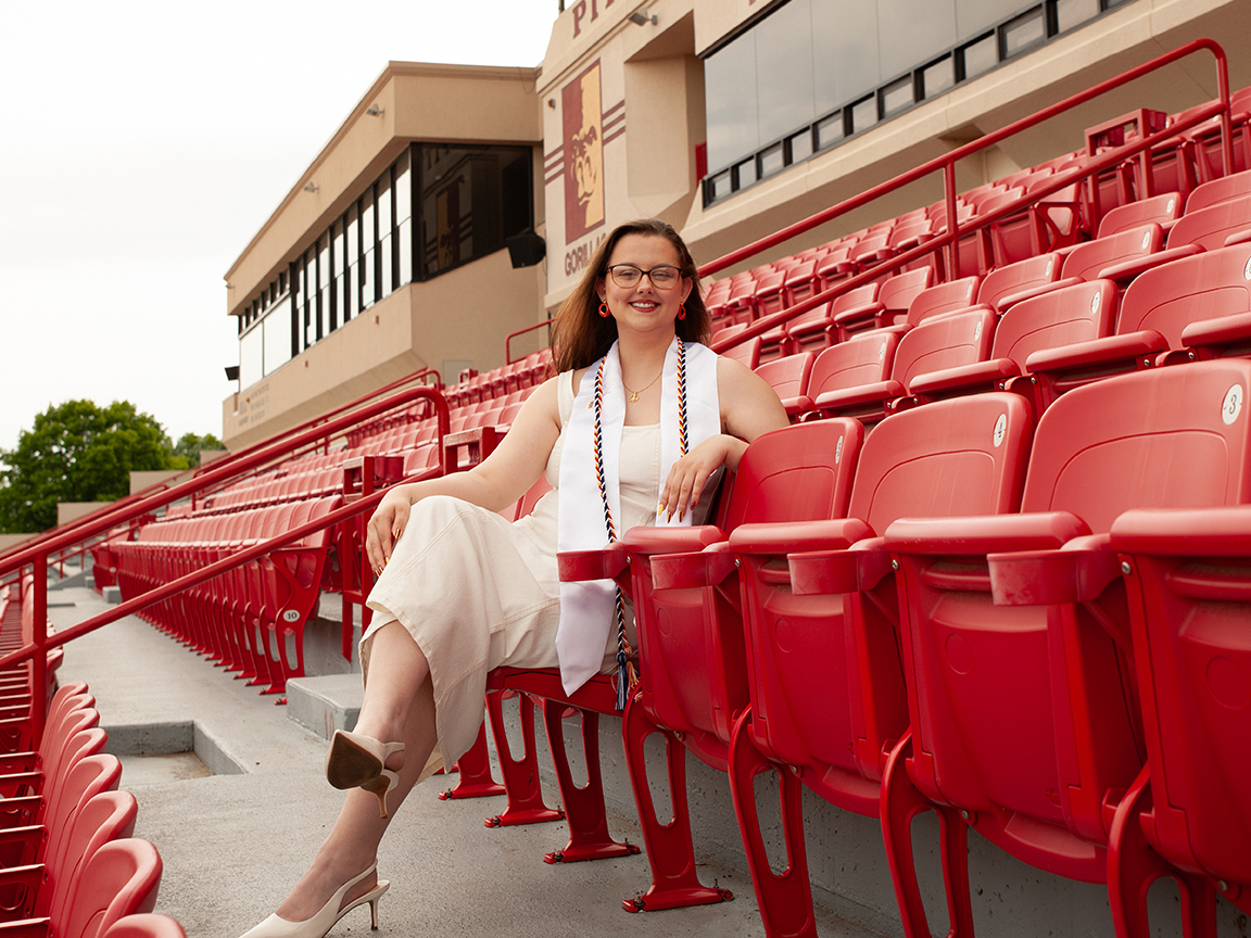 Rebekah poses in carnie smith stadium seats at Pittsburg State, wearing her graduation cords and stole