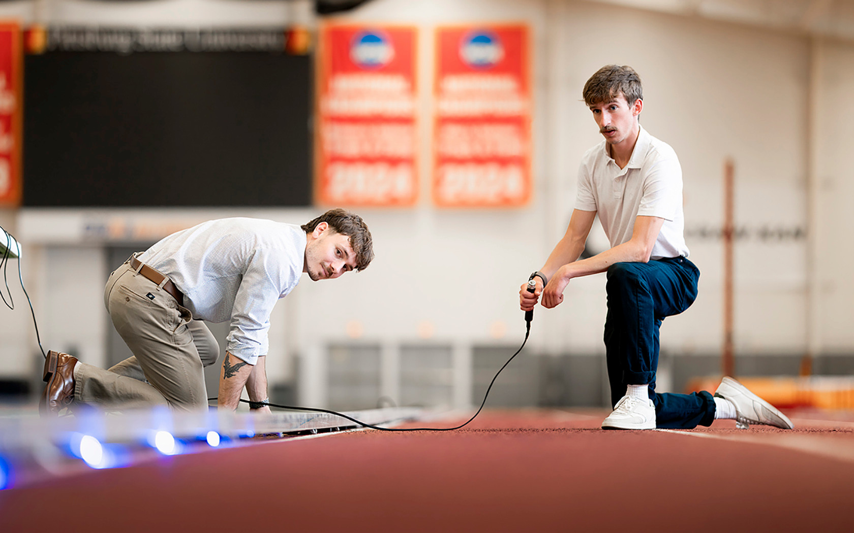 2 senior males install pacer lights on the indoor track and field