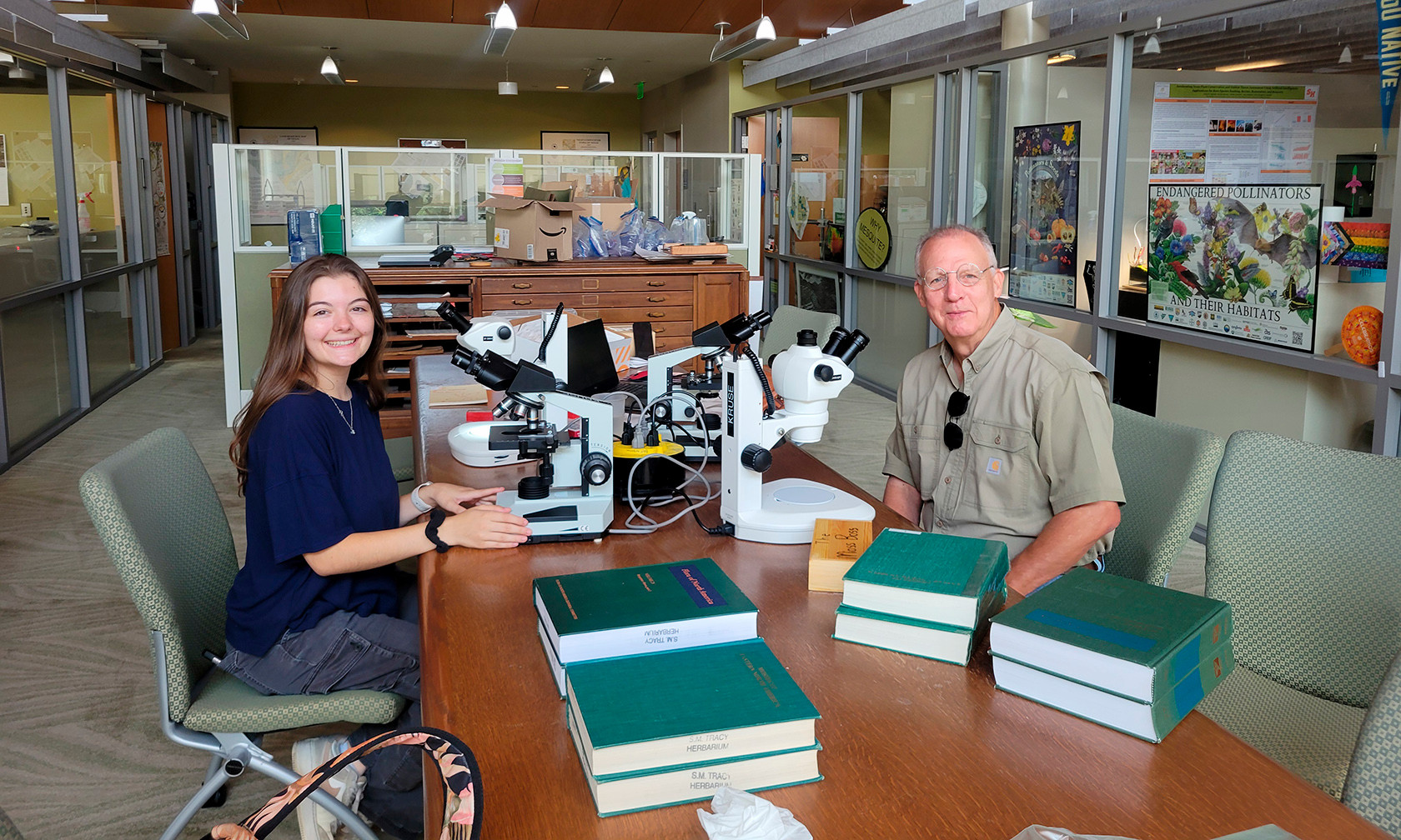 intern and scientist sitting at table with microscopes