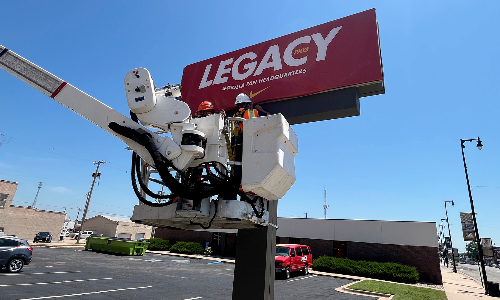 Two workers in a bucket truck install a large red sign in front of a building