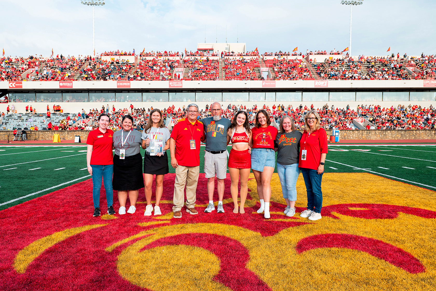 Members of the family pose on the field with Pitt State staff members holding awards on the football field 