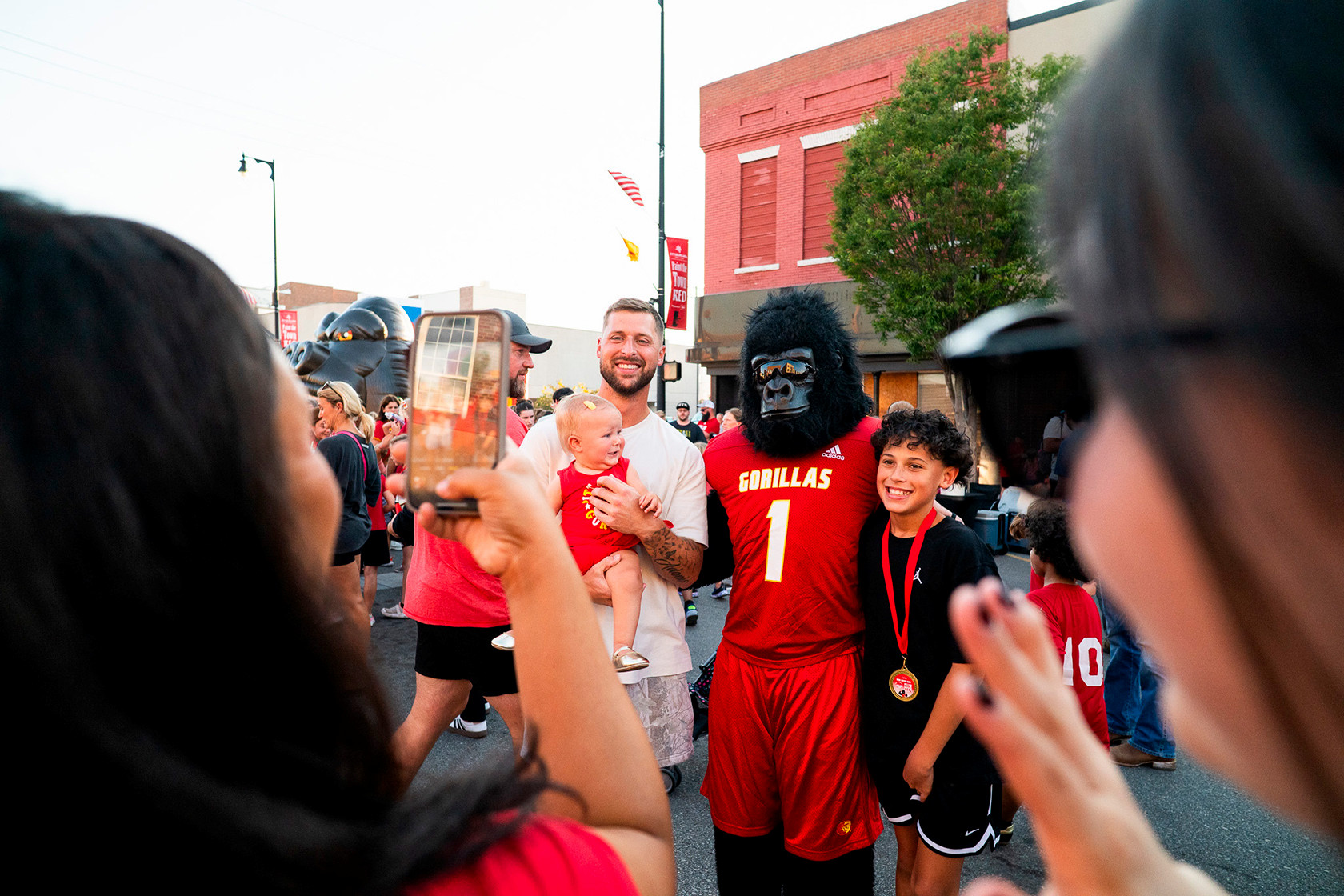 A mom takes a cell phone shot of gus the gorilla posed up with a father holding a baby, and a son on the other side