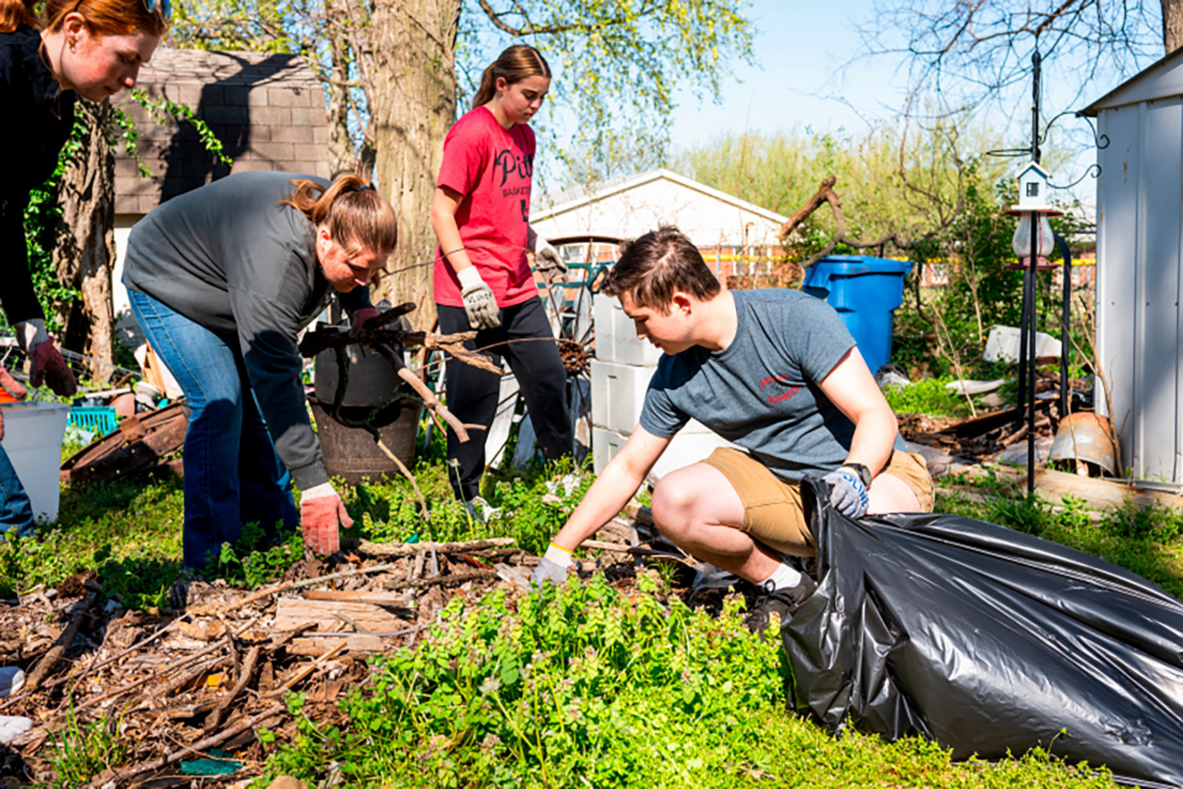 Students gather sticks into trash bags in someones yard